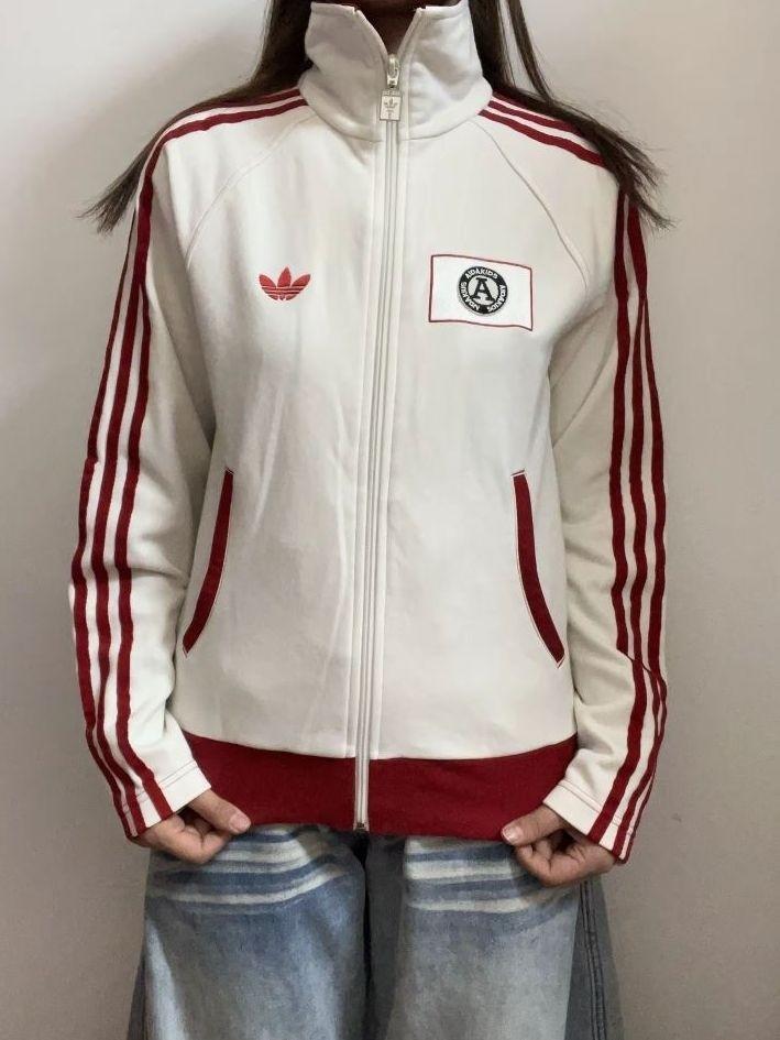 这是一件 adidas Originals(三叶草) 的复古运动夹克,经典的白红配色与胸前的徽章设计